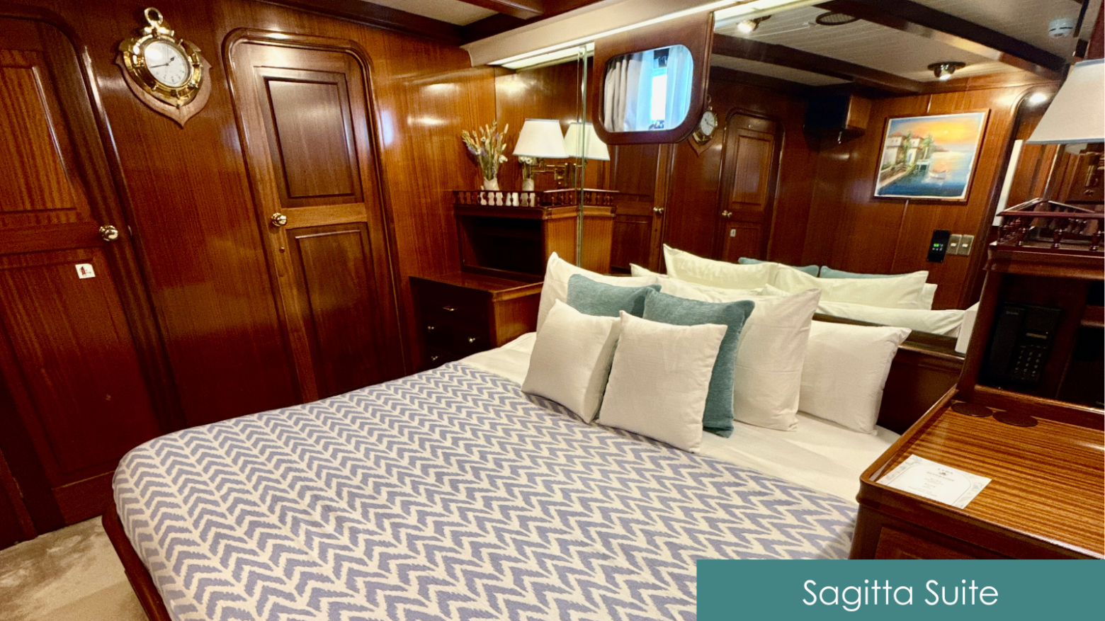 Luxurious ship cabin with wood paneling, bed with blue pattern blanket, and decorative pillows.