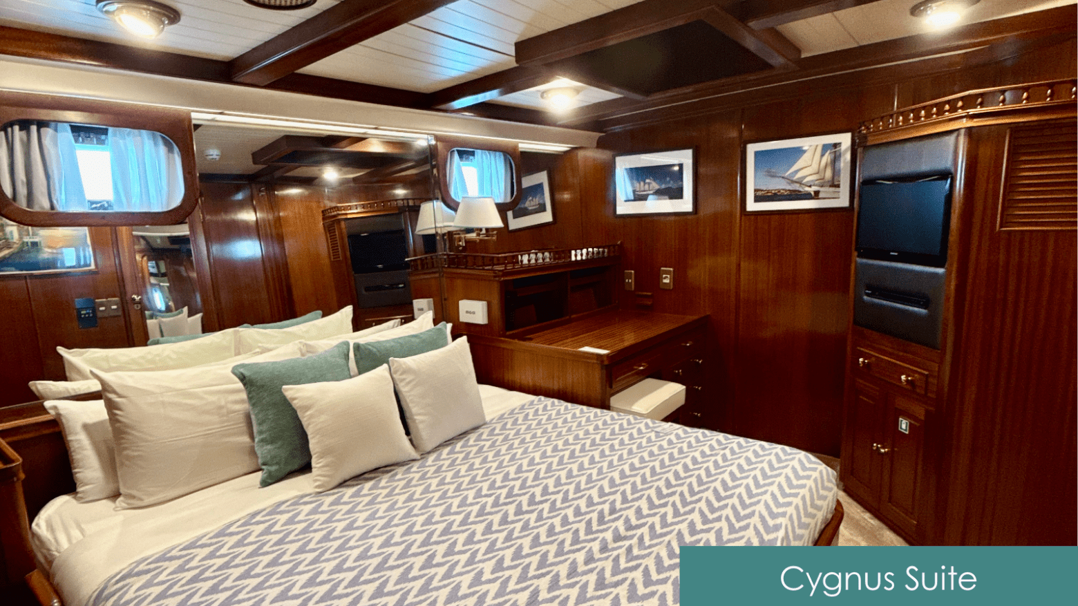 Luxurious wood-paneled suite with bed, pillows, desk, and framed sailboat photos.