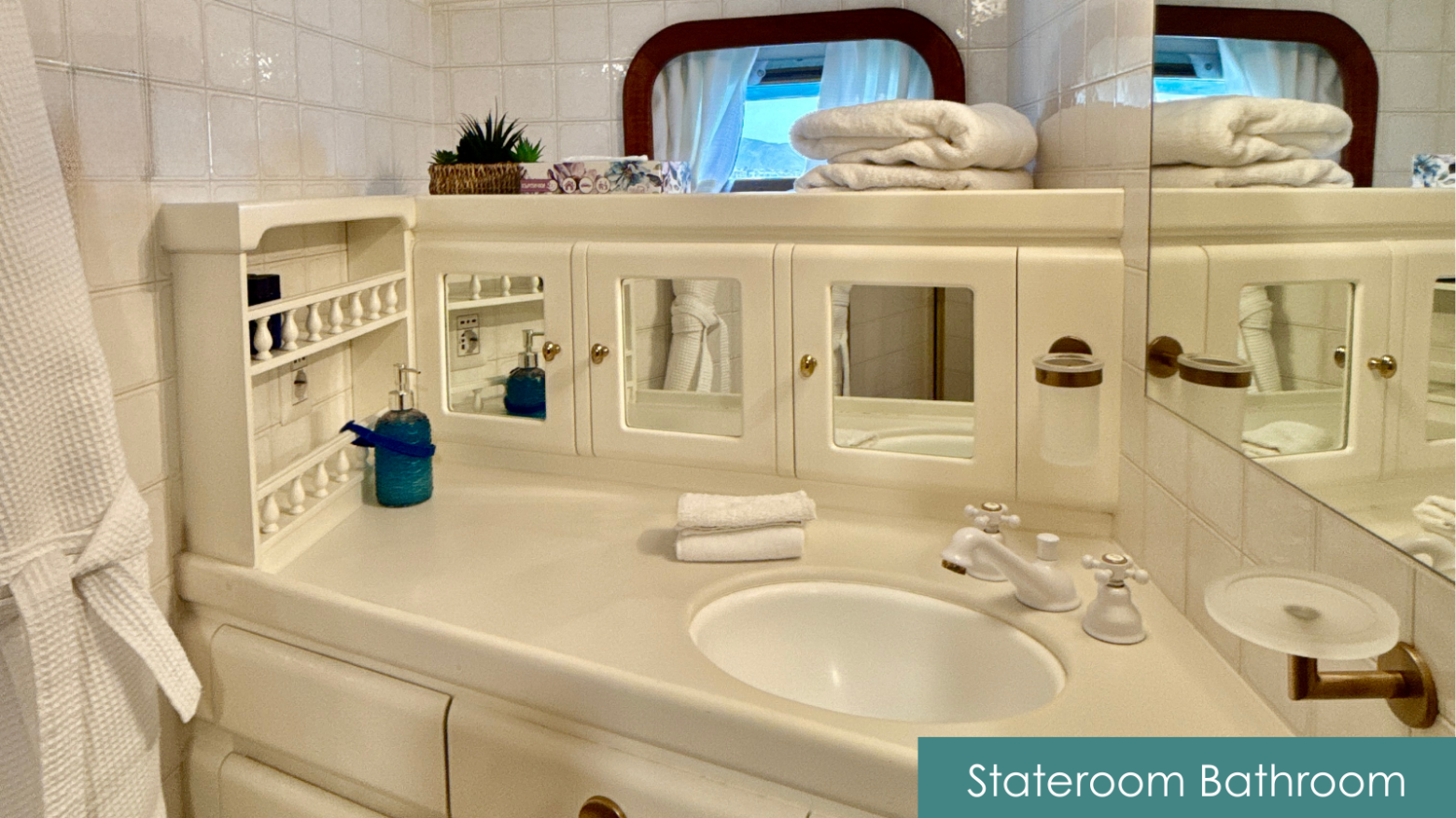 White bathroom with mirror cabinets, sink, towels, and toiletries in a stateroom.