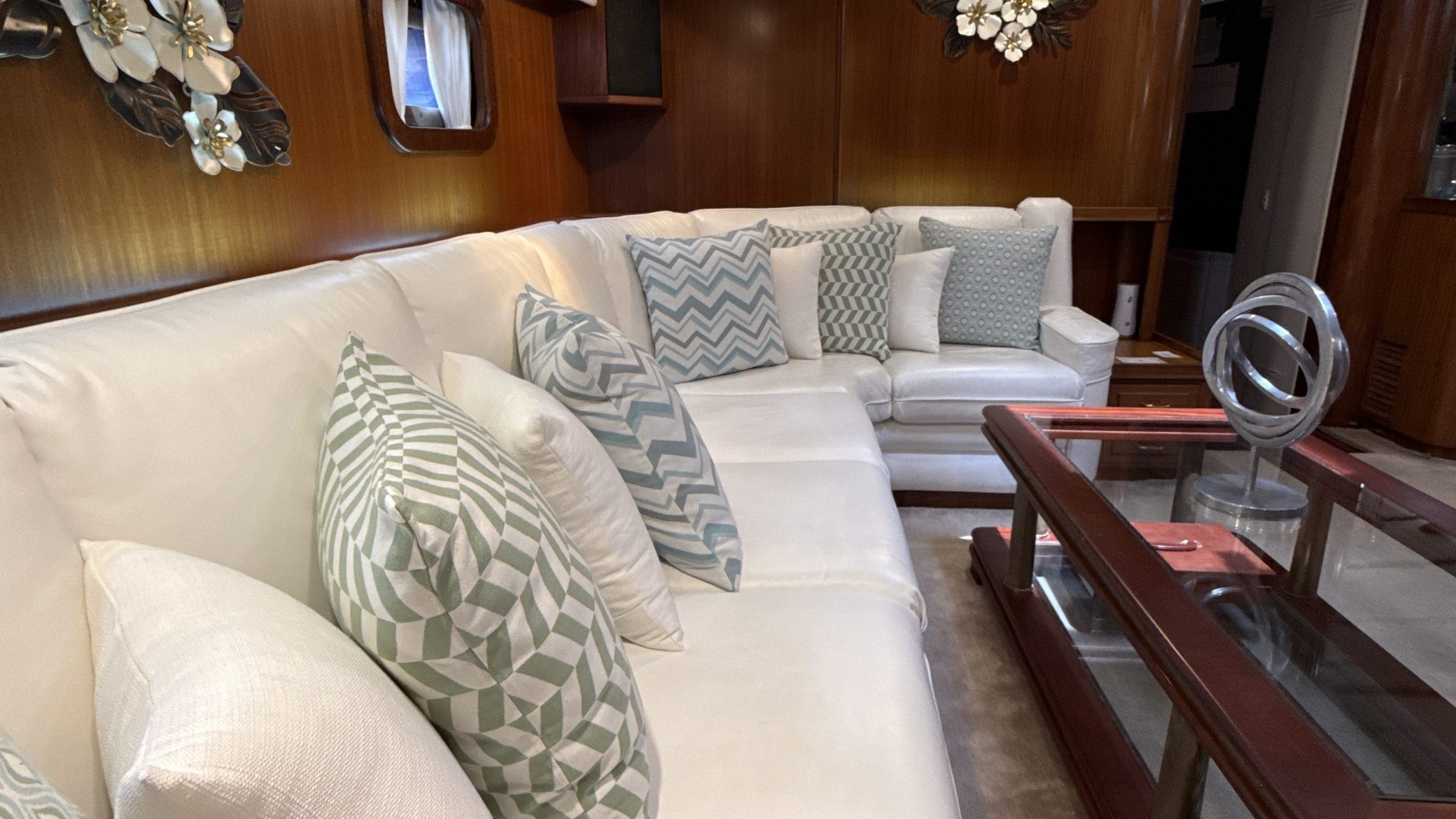 Boat interior with white sofa, geometric cushions, wooden walls, and decorative floral wall art.