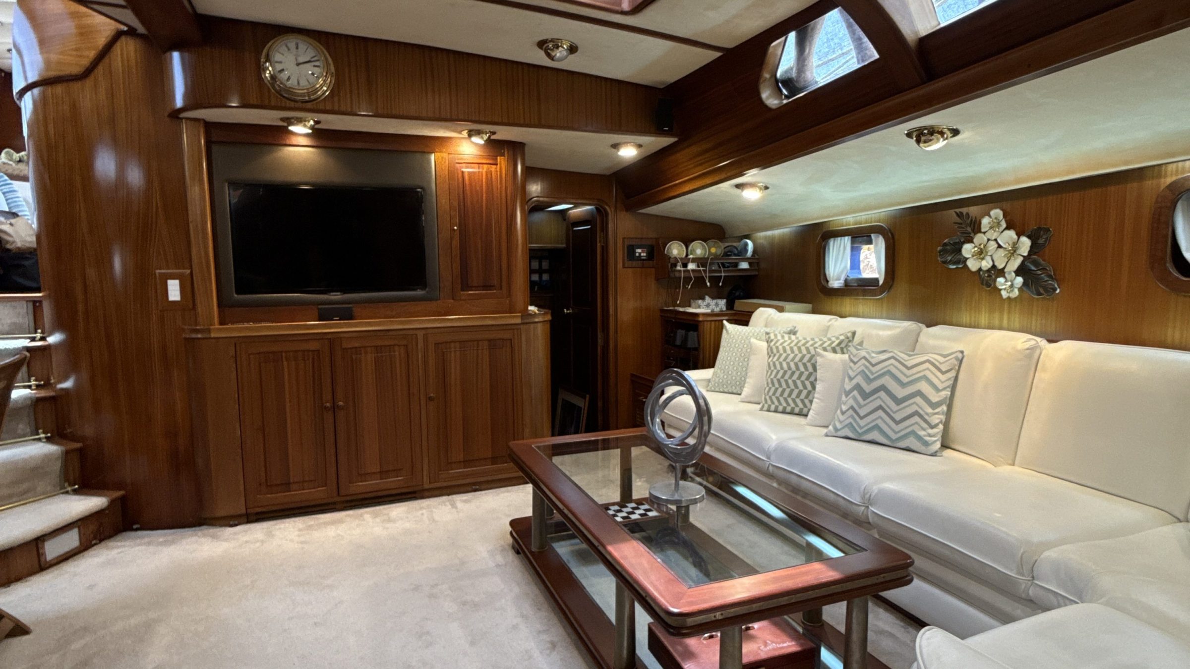 Luxurious yacht interior with wooden panels, white couch, glass table, and wall-mounted TV.