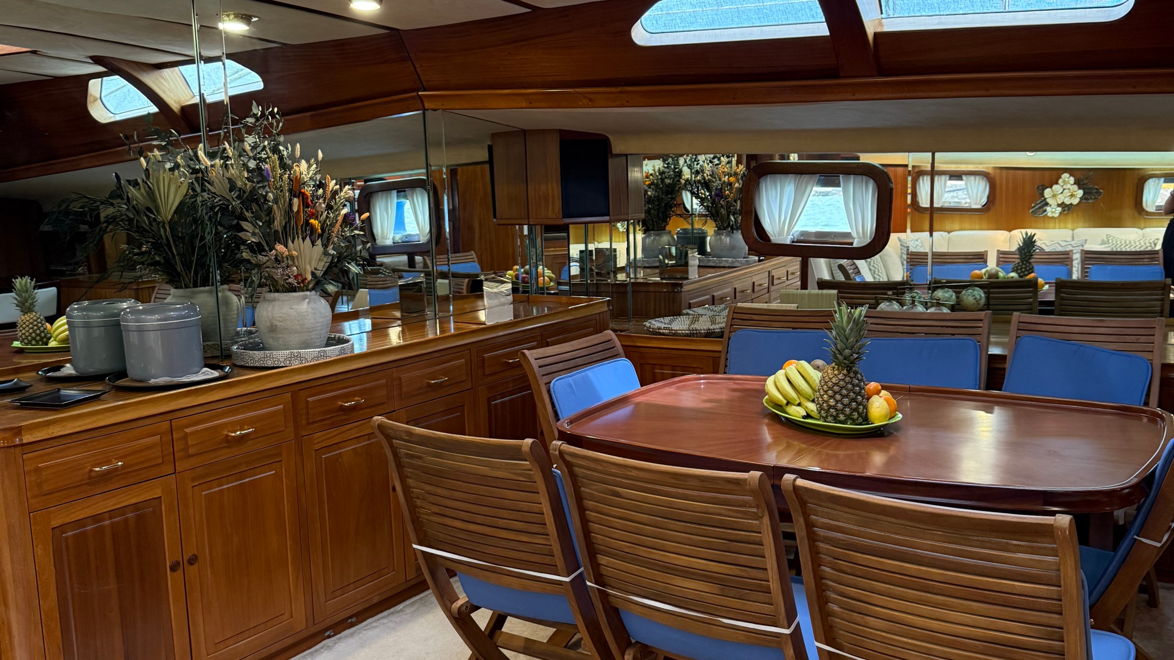 Wooden dining area in yacht with blue cushioned chairs and skylight above.