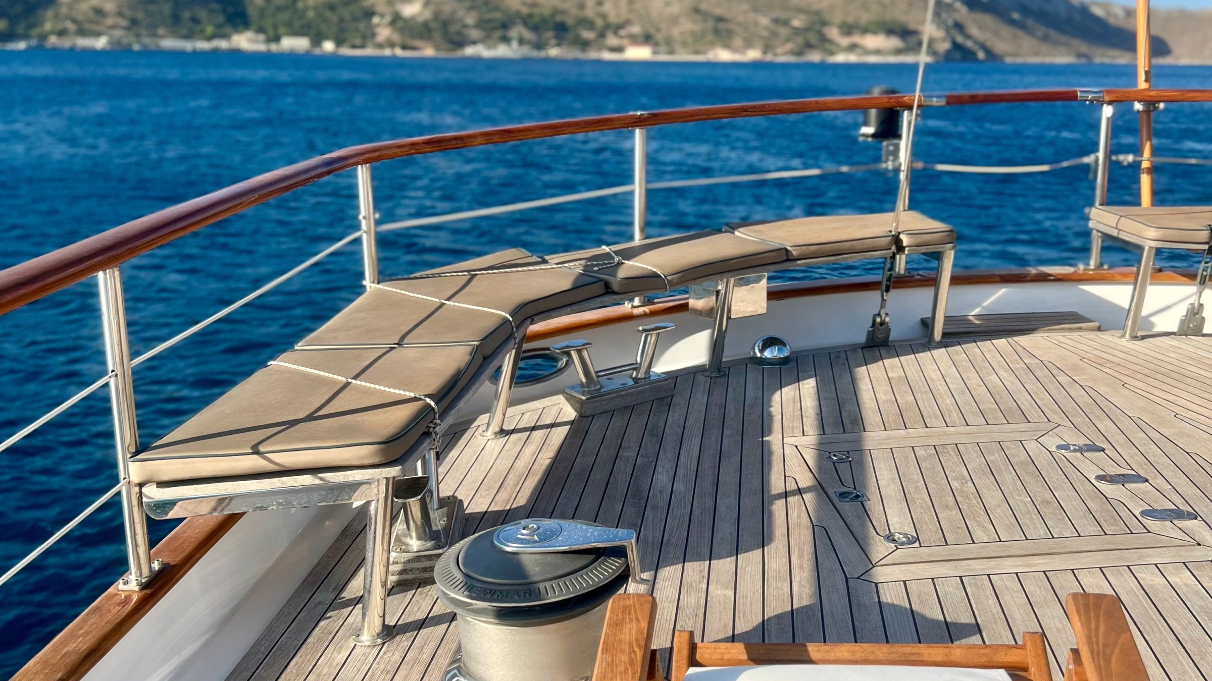 Boat deck with chair, seating, red flag, and mountain view across the water.