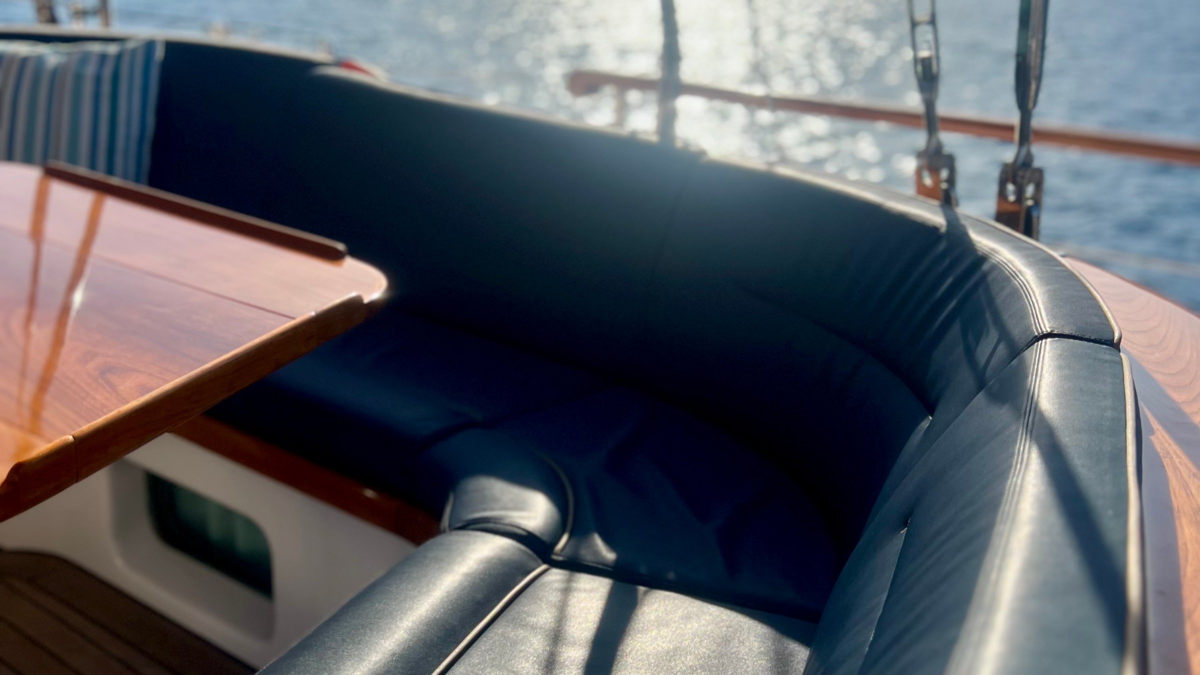 Boat seating area with leather cushions, wooden table, and sunny ocean view.