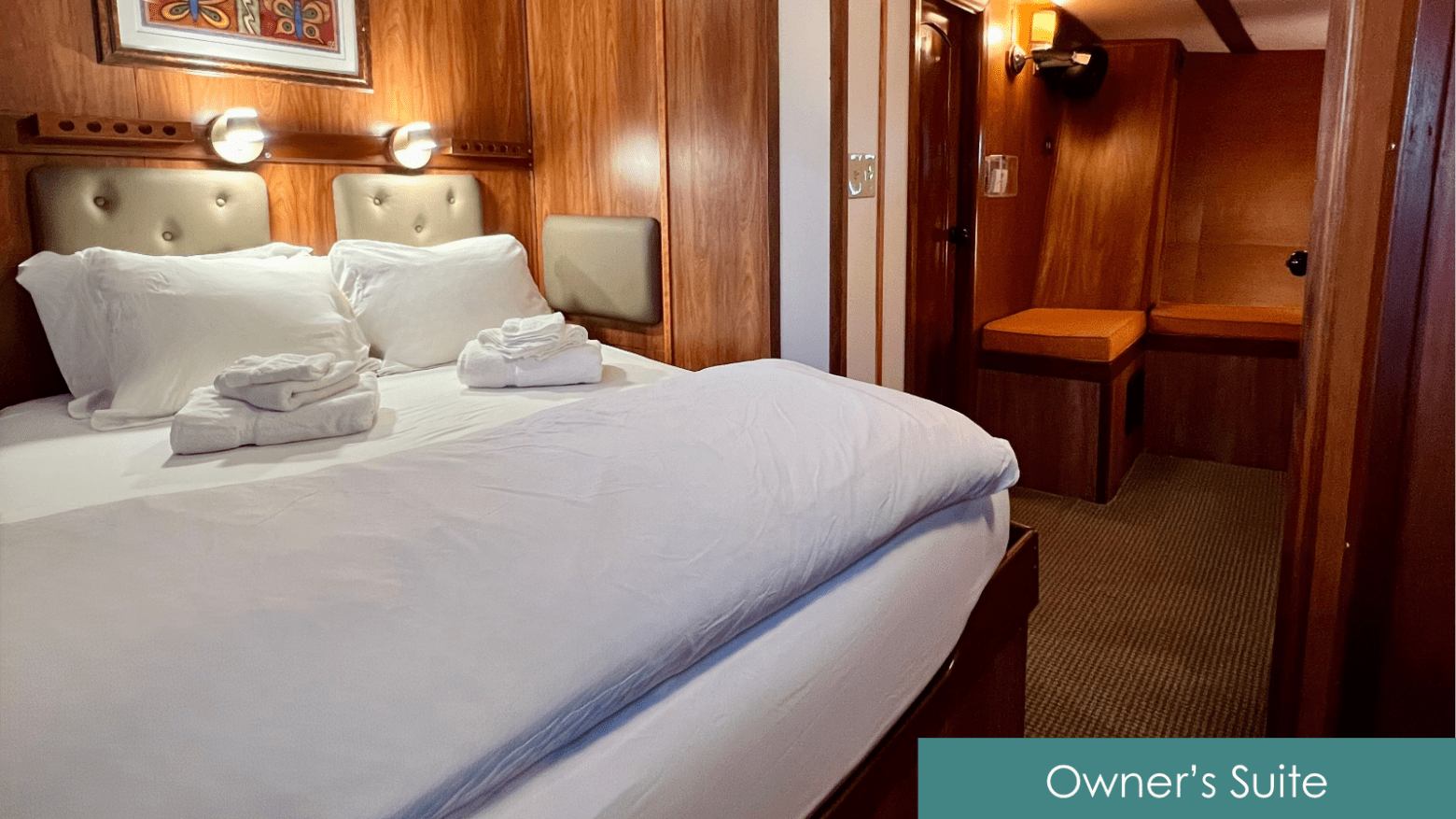 Cozy wooden cabin with double bed, white linens, two folded towels, and warm lighting.