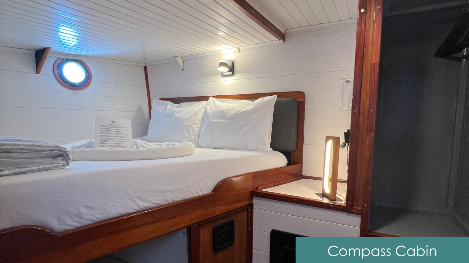 Cozy cabin room with a neatly made bed, porthole, and soft lighting.