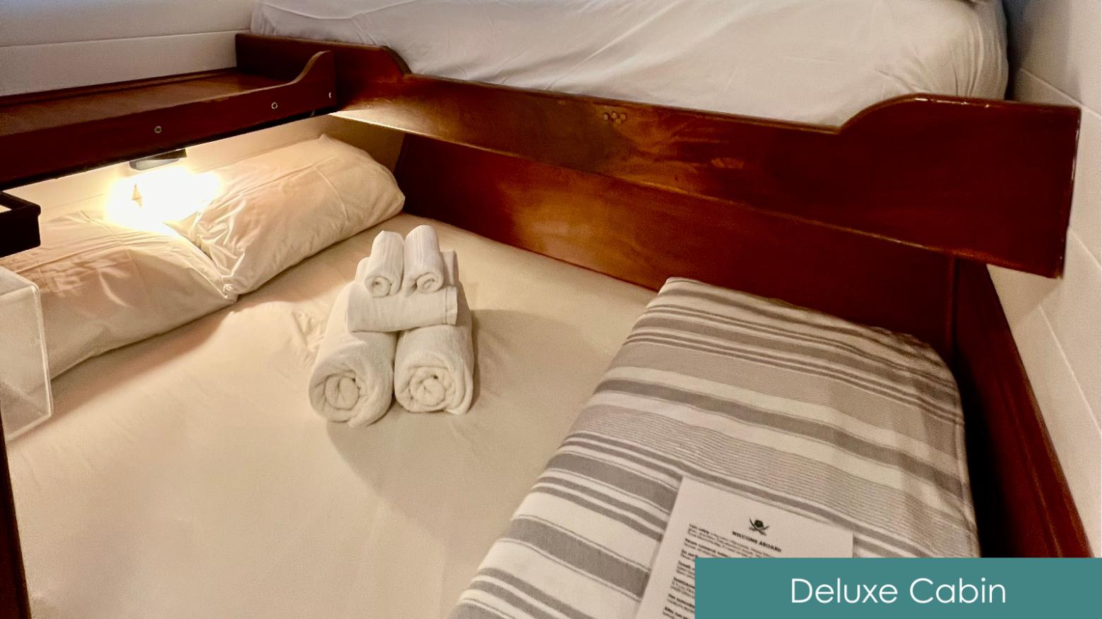 Small cabin bed with striped sheets, rolled towels, and a soft light.