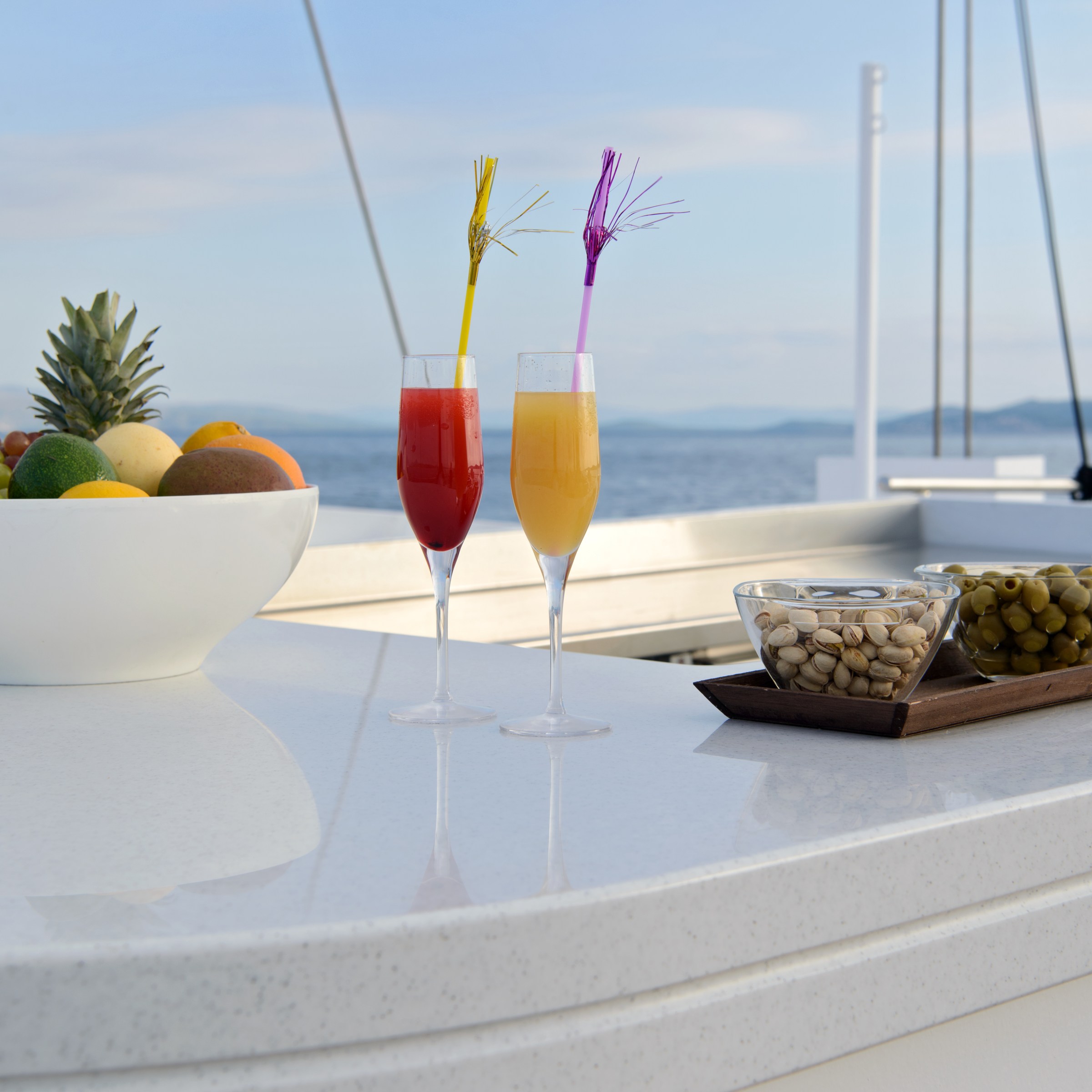 Outdoor bar on yacht with fruit bowl, two drinks, nuts, and olives.