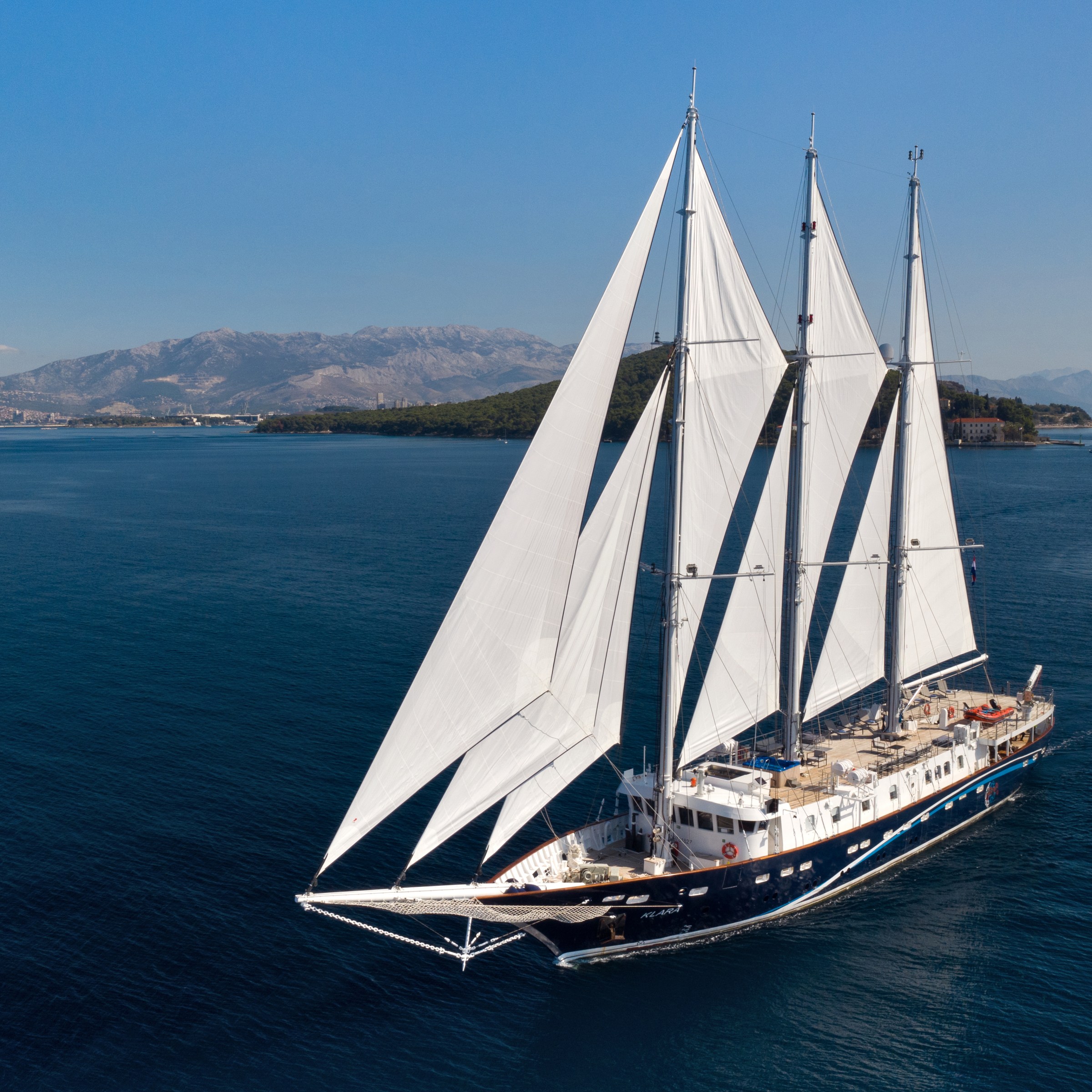 Large sailing ship with three masts on calm blue sea under clear sky.