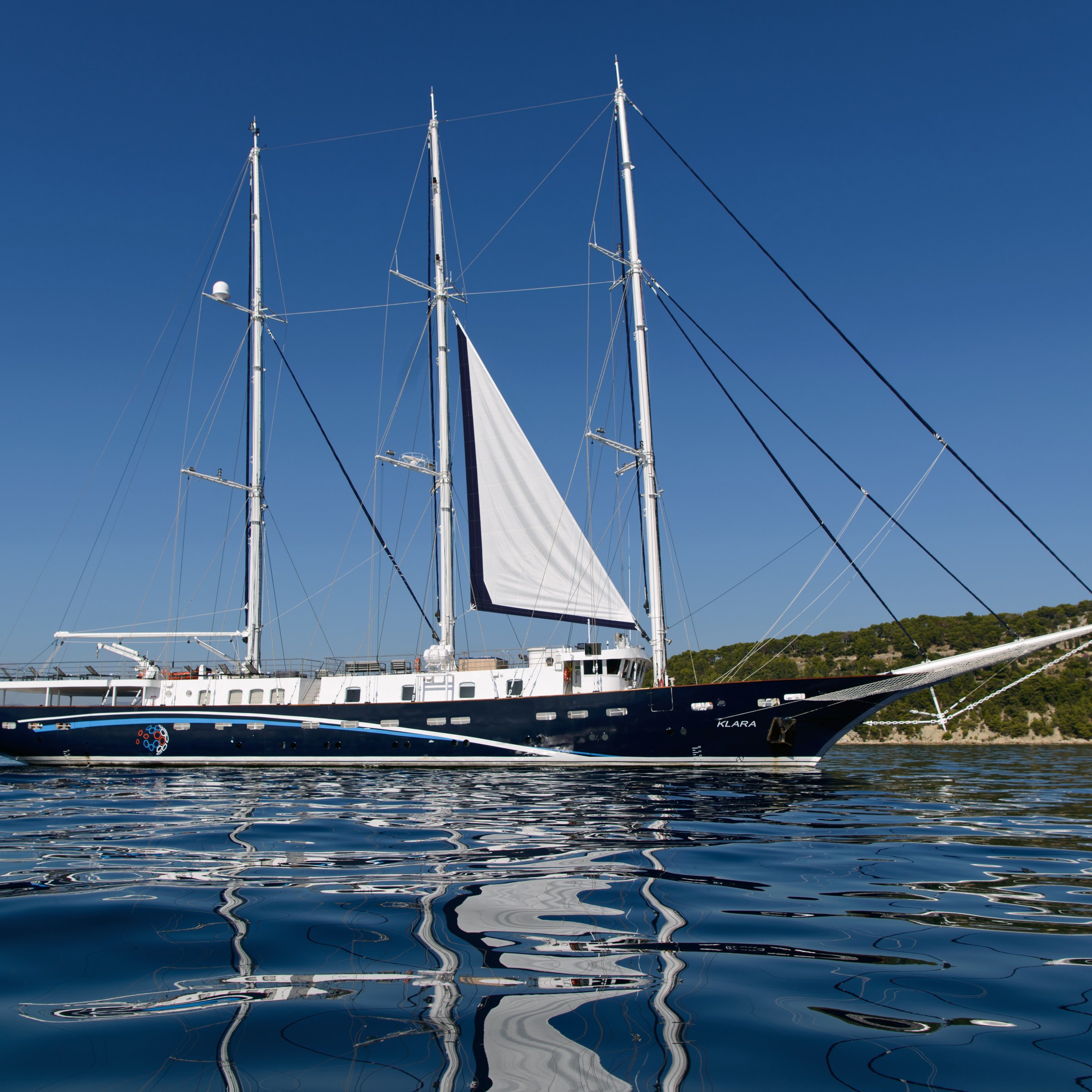 Large sailing yacht with multiple masts on calm water against a clear blue sky.