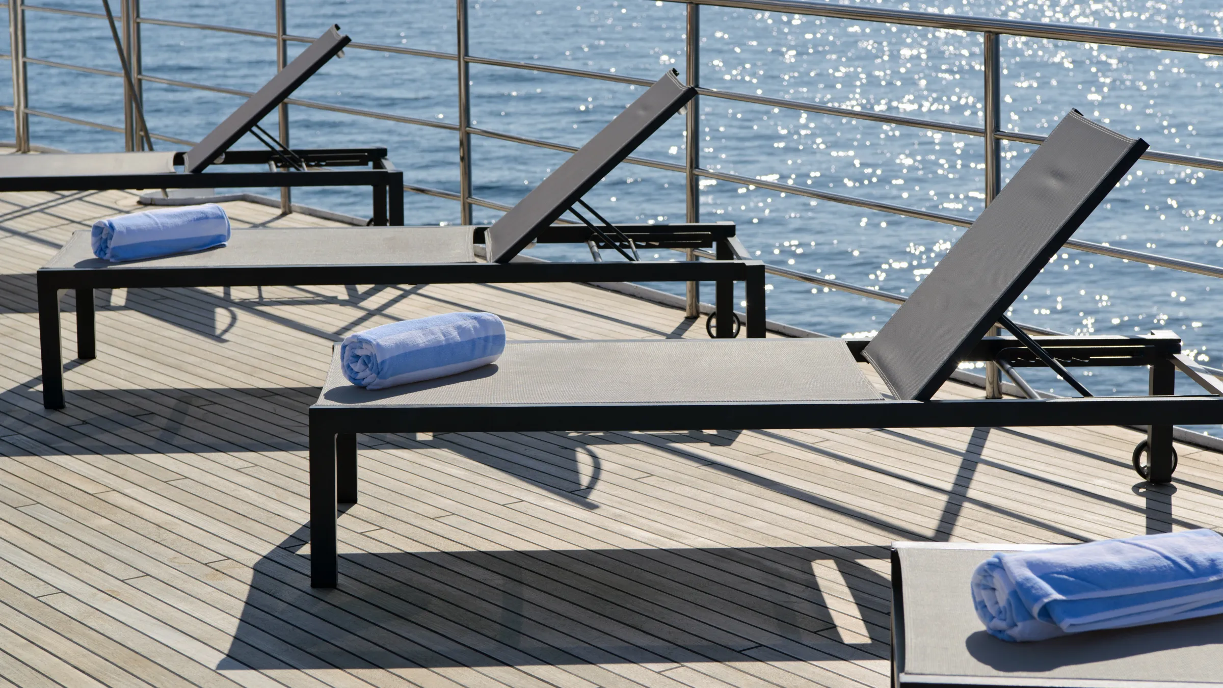 Sun loungers with blue towels on a deck overlooking sparkling water.