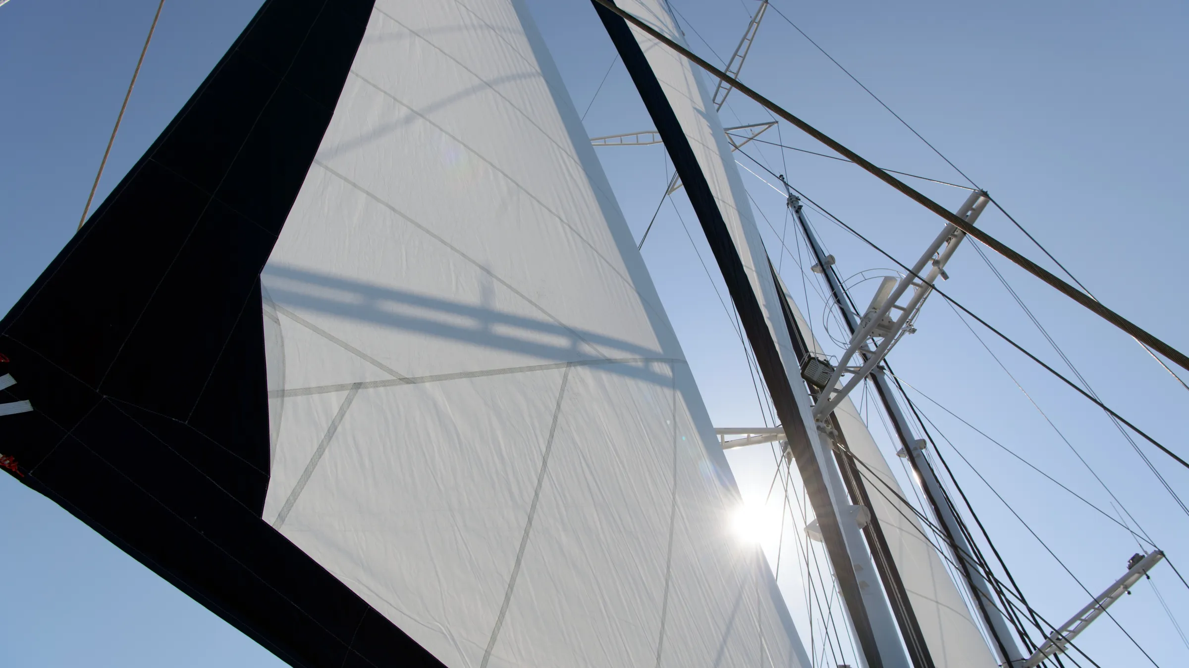 Close-up of a sailboat's sails with sunlight shining through against a clear blue sky.