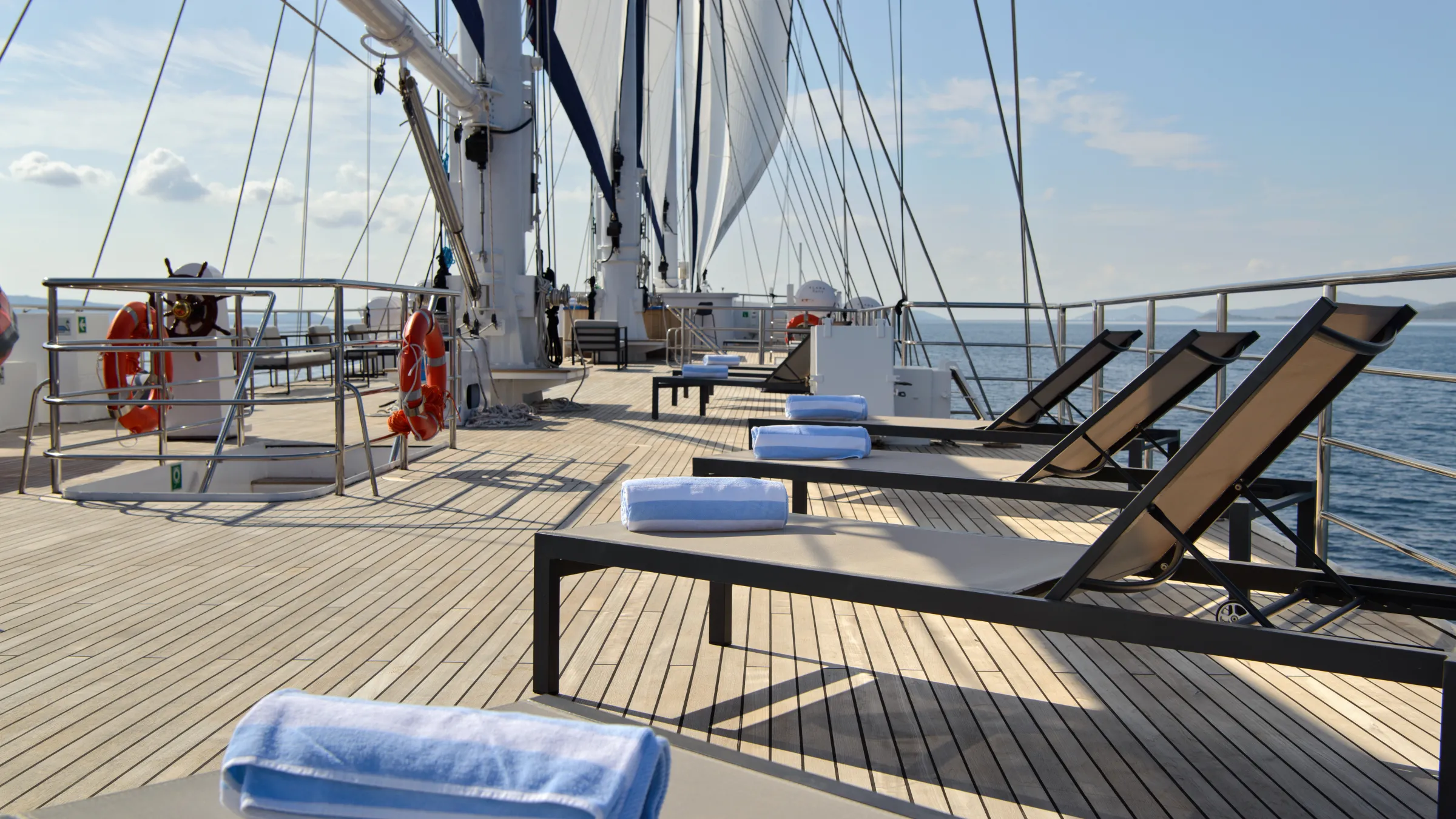 Deck of a sailboat with sun loungers and neatly rolled towels.