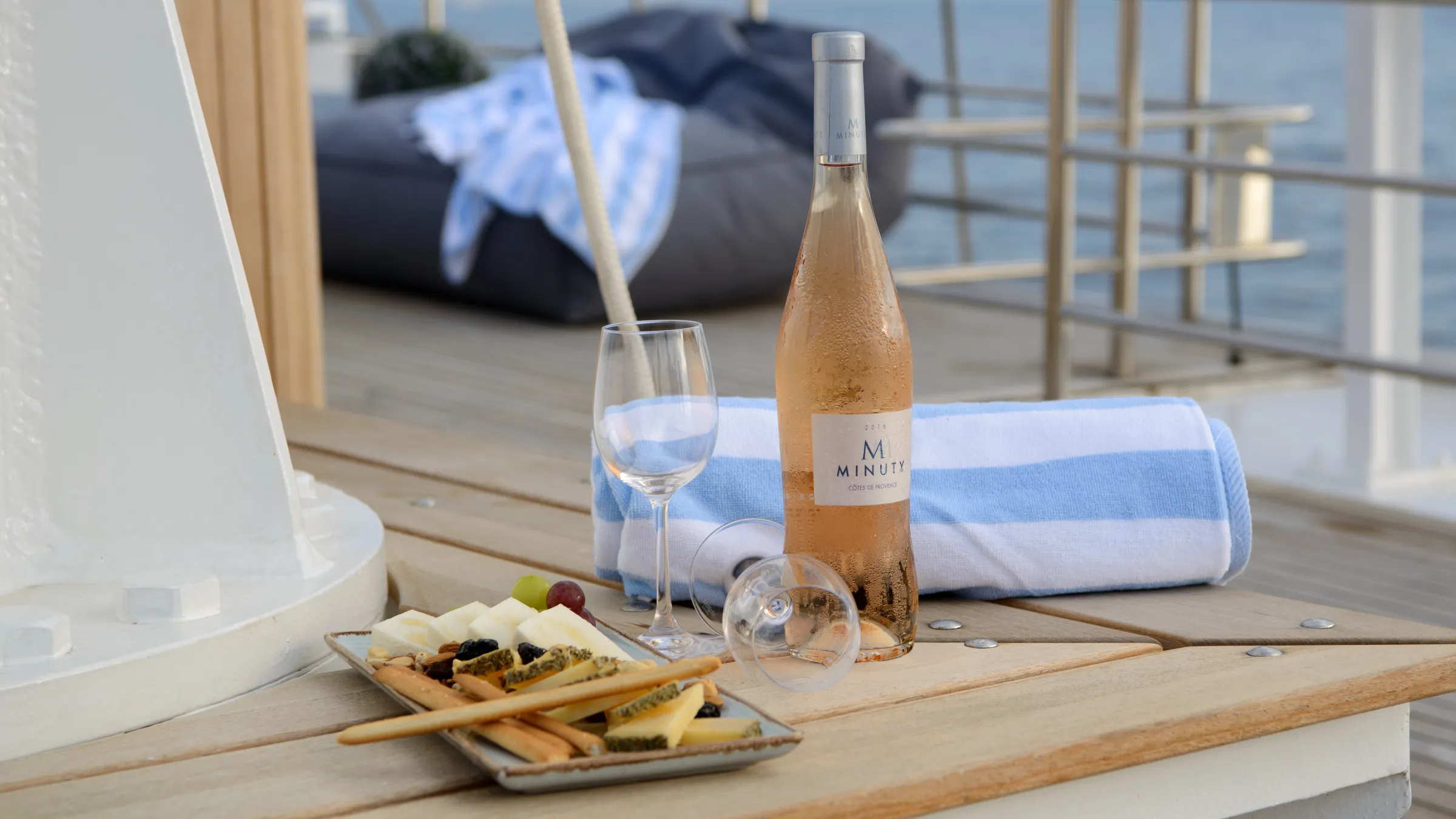 Wine bottle, glass, and cheese platter on a boat deck.