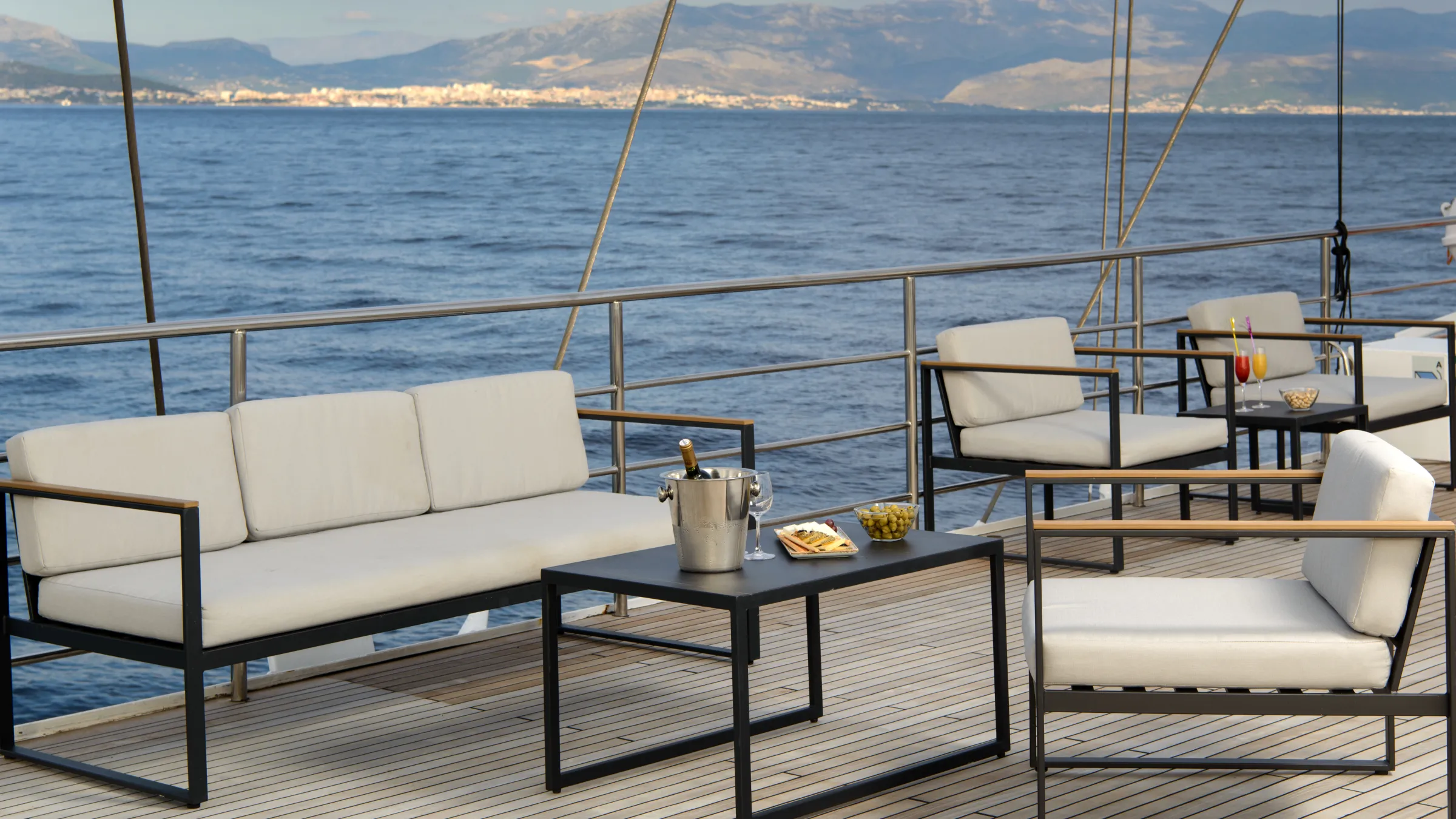 Outdoor patio furniture set on a deck by the sea with mountains in the distance.