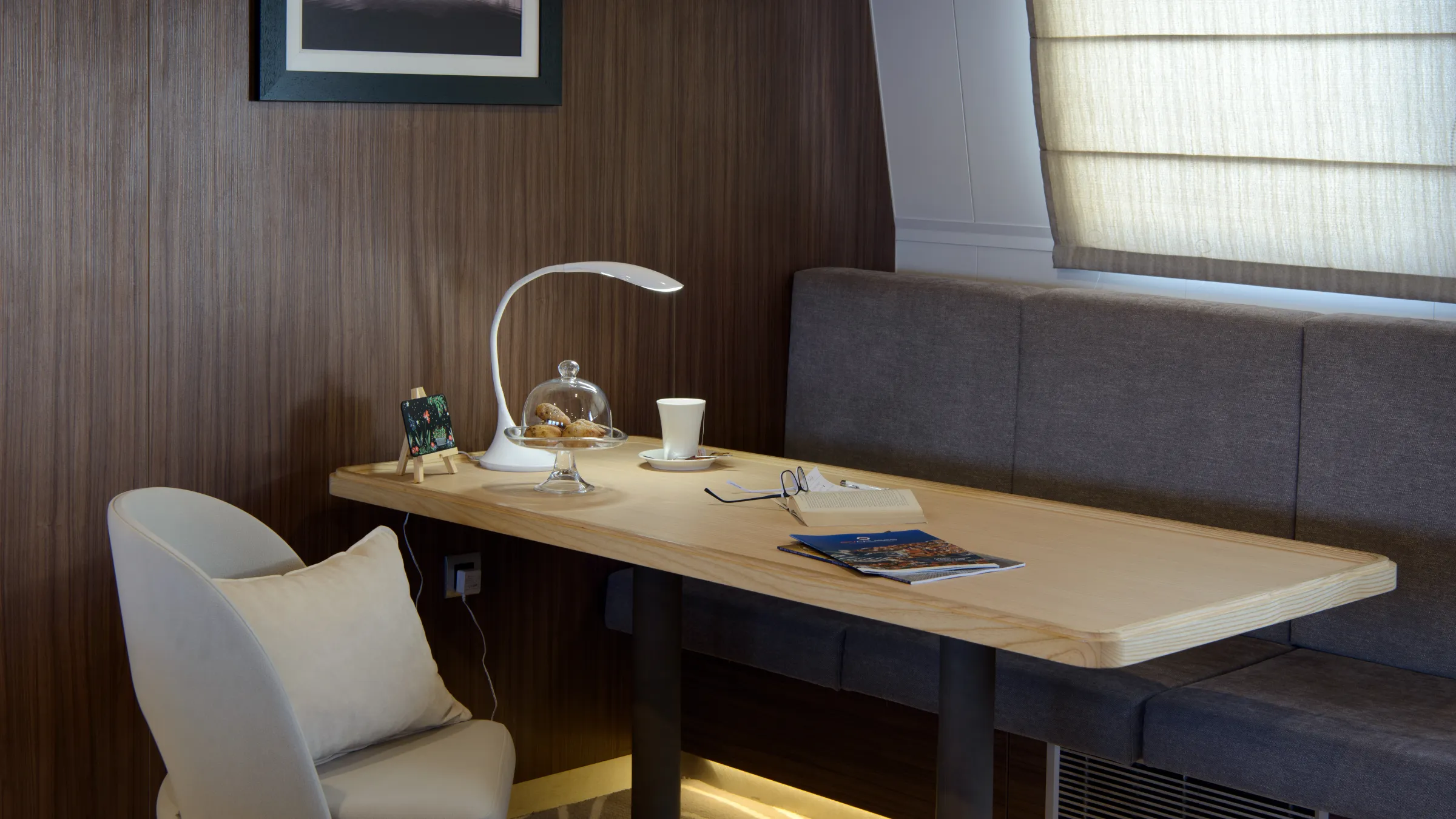 Elegant hotel room with desk, lamp, chair, couch, and framed photo.