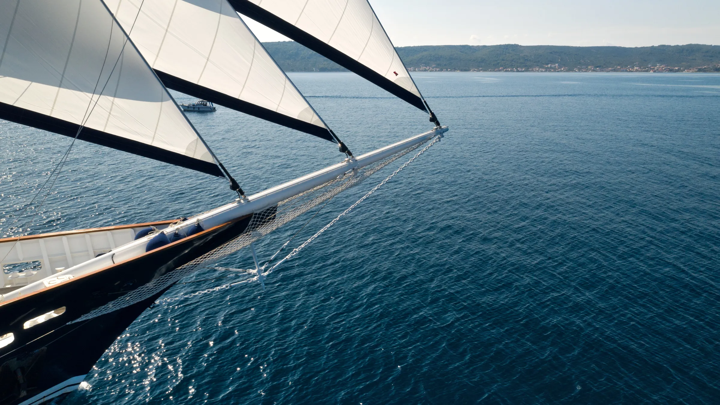 A sailboat with white sails gliding on calm blue water near a distant coastline.