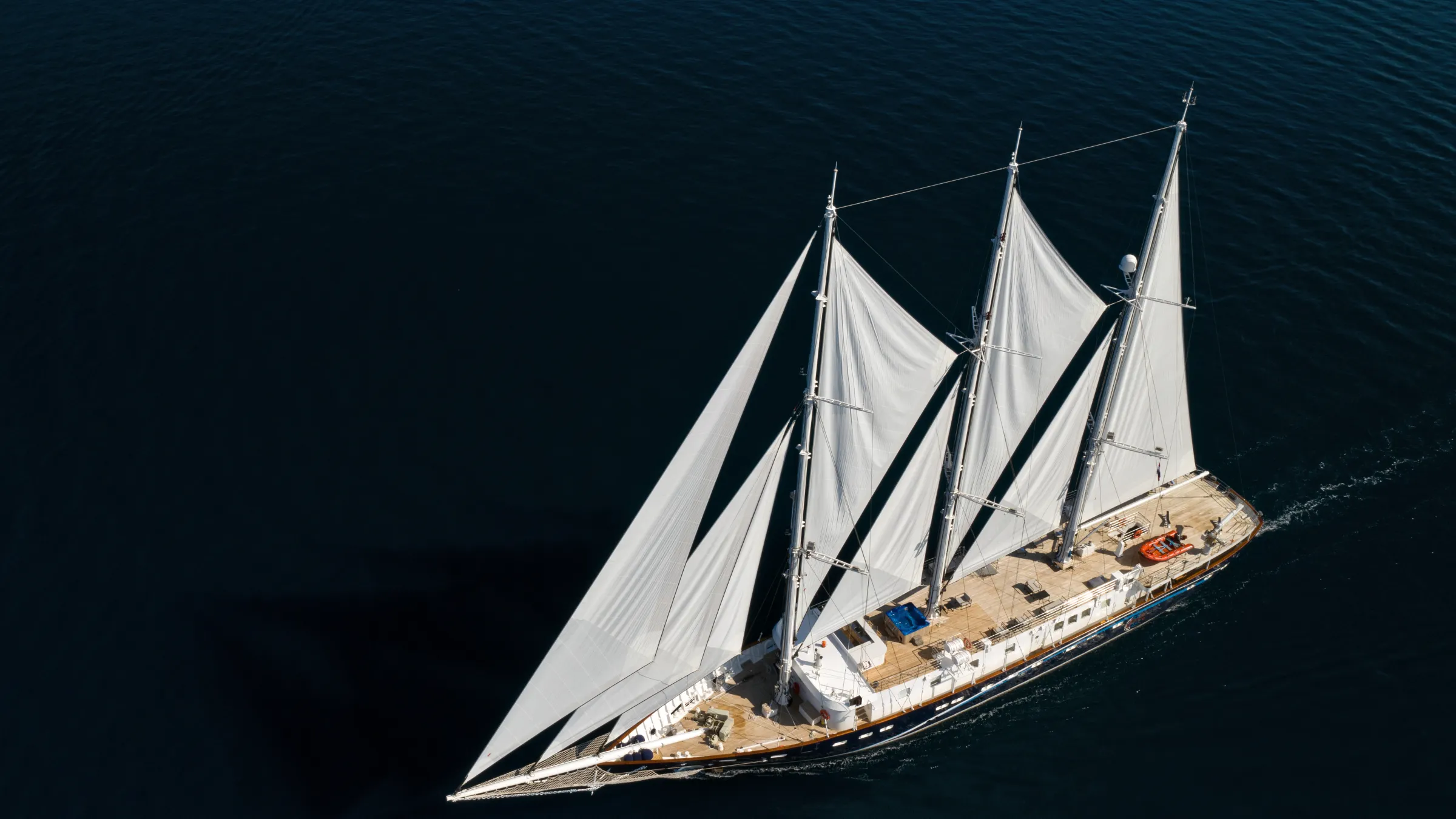 Aerial view of a large sailing ship with three masts on dark blue water.