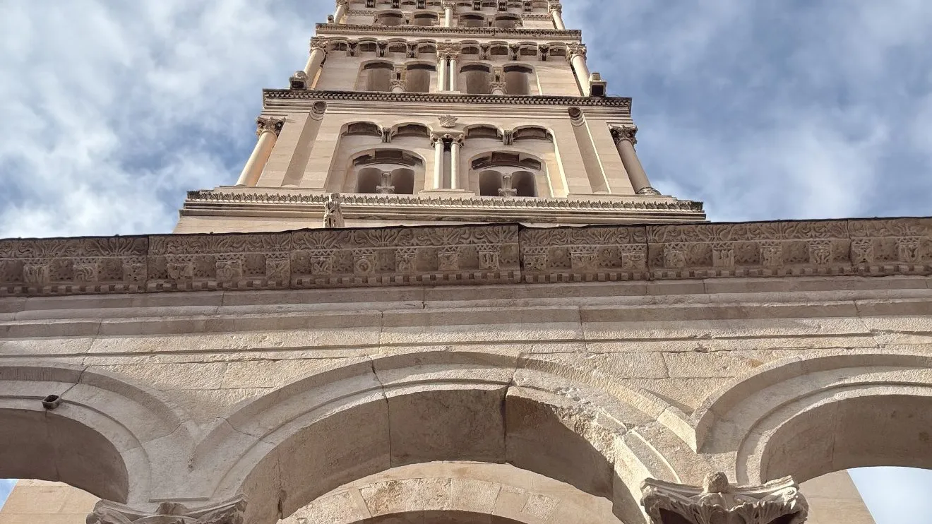 Low-angle view of a historic stone tower with arches, against a cloudy sky.