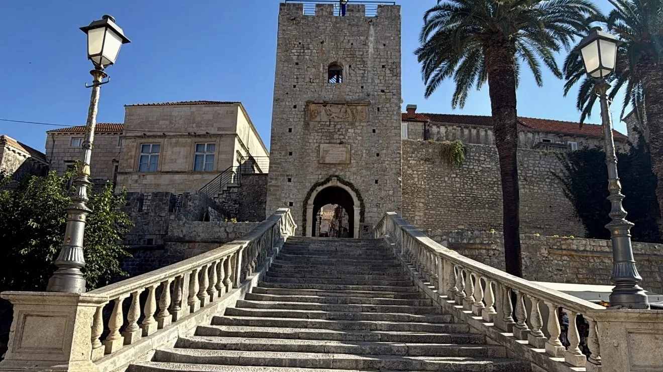 Stone staircase leading to a historic building with a tower and palm trees.