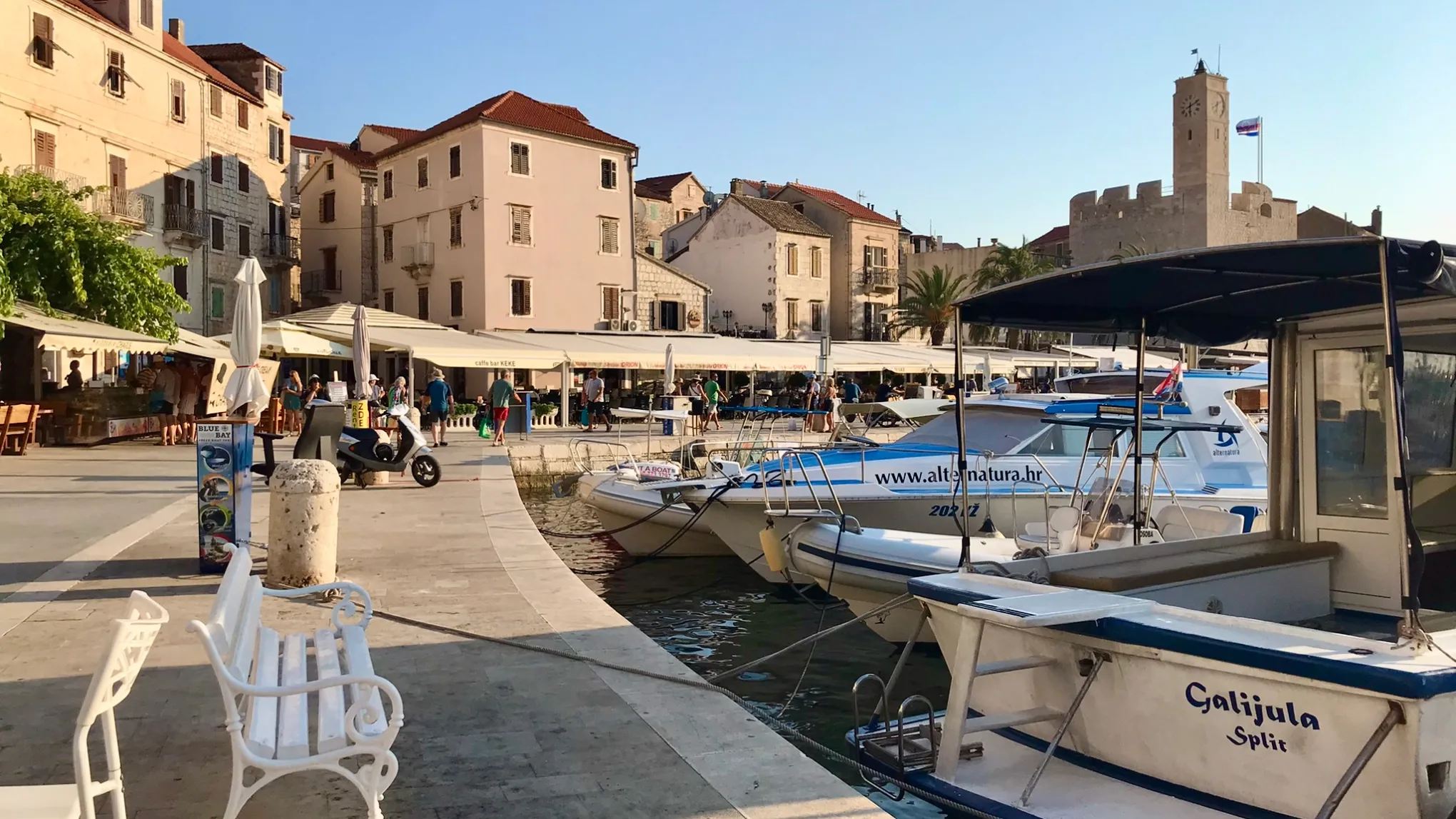 Boats docked at a sunny harbor with a historic town in the background.