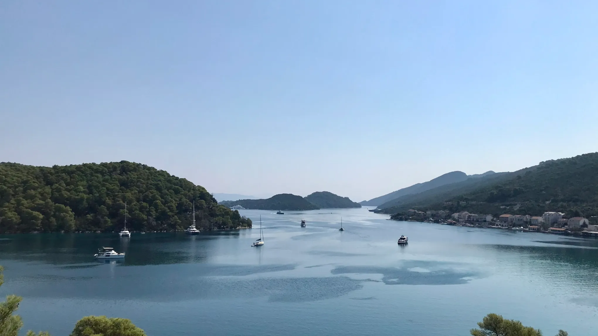Calm bay with sailboats and green hills on a clear day.
